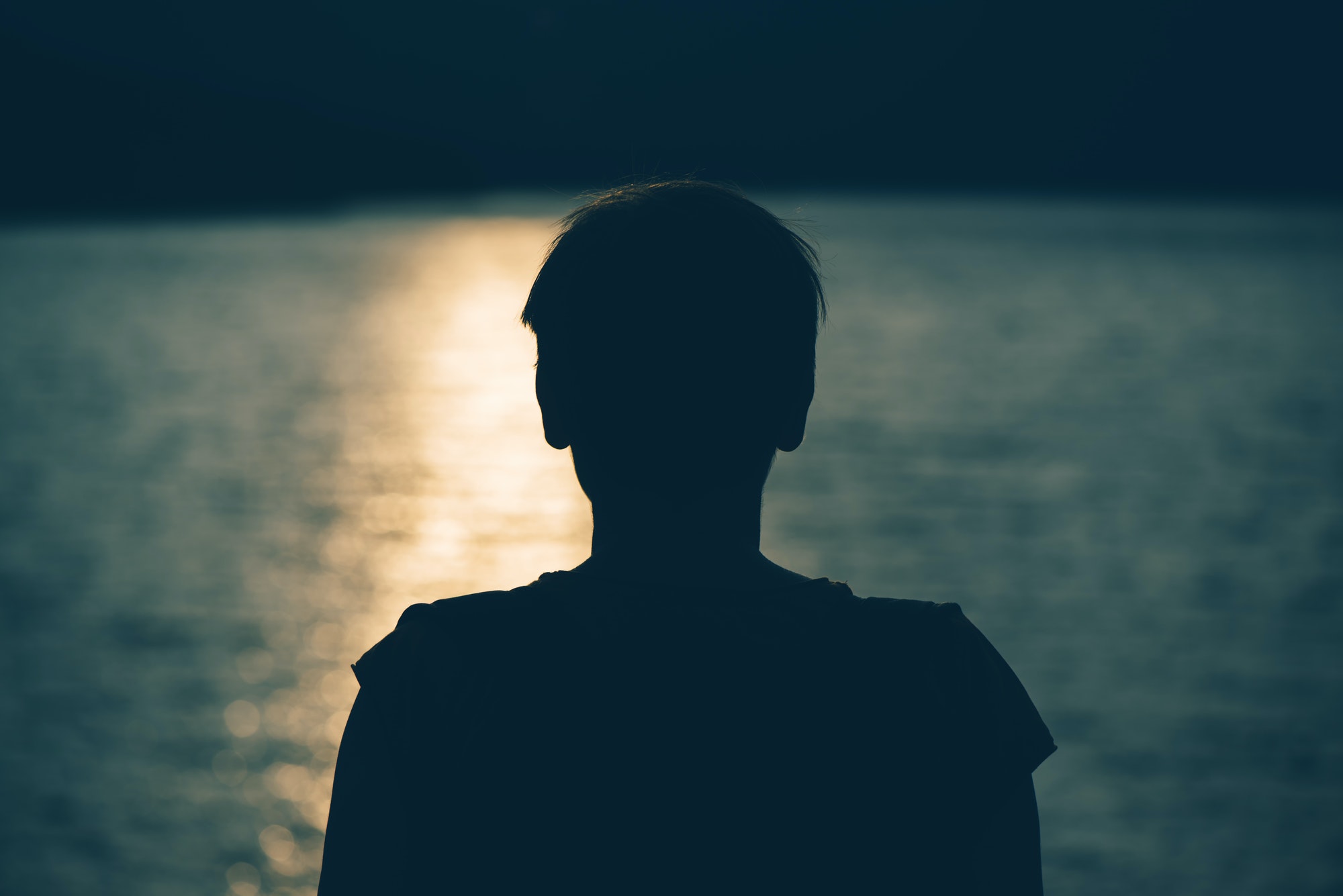 Silhouette of depressed sad woman standing by the lake